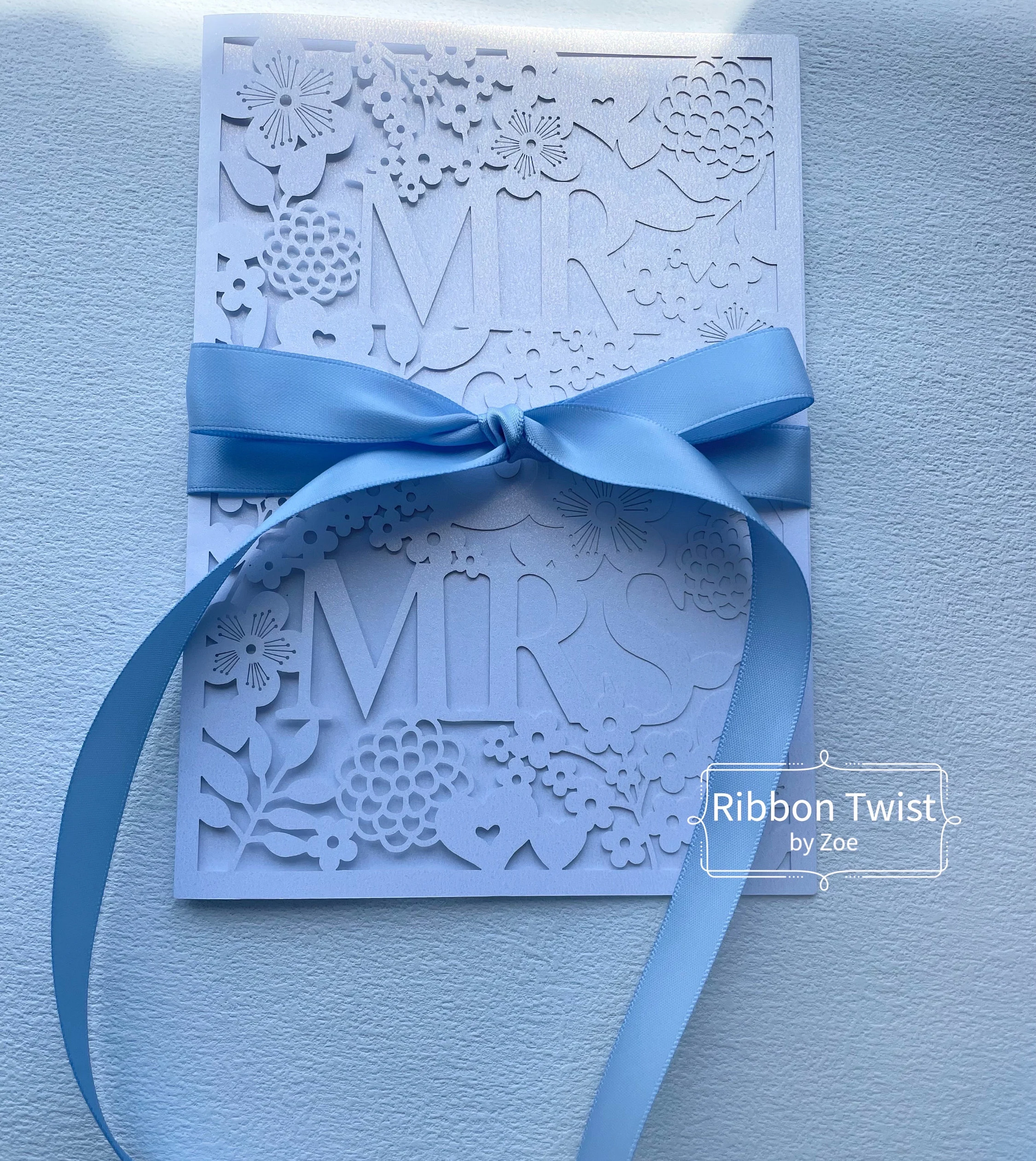 Sky blue satin ribbon tied around a white floral invitation